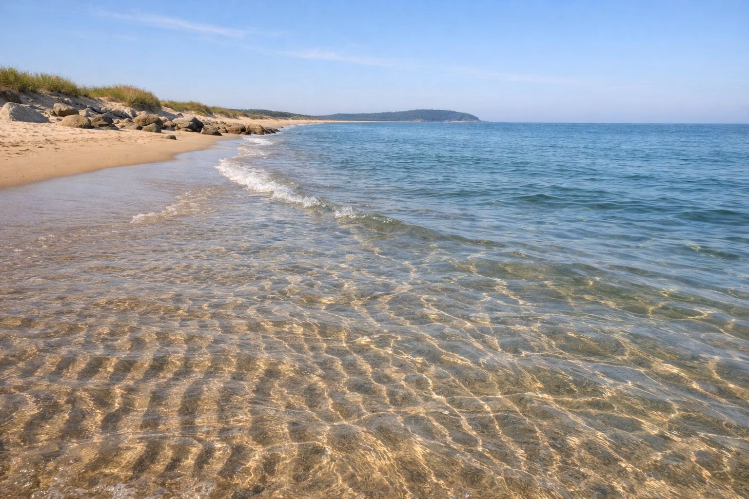 Clear shallow ocean water over rippled sand at the waterline on a summer morning