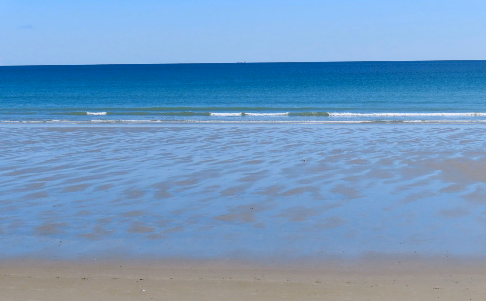 Blue-green ocean water beyond golden sand on Nantasket Beach on a clear morning